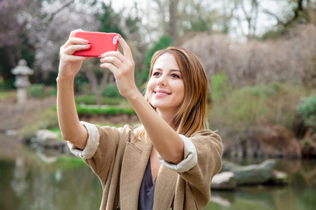 Redhead girl making selfie with mobile phone in a park in spring timeの写真素材