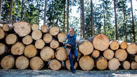 Mother and child in backpack standing near sawn logs in the forestの写真素材