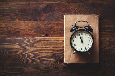 Little alarm clock and books on wooden background. image in old color style