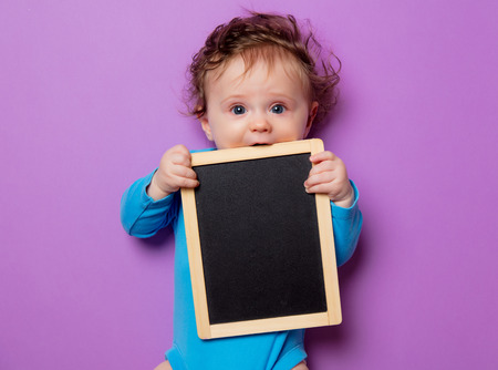 little infant baby with hair and blackboard lying down on purple backgroundの写真素材