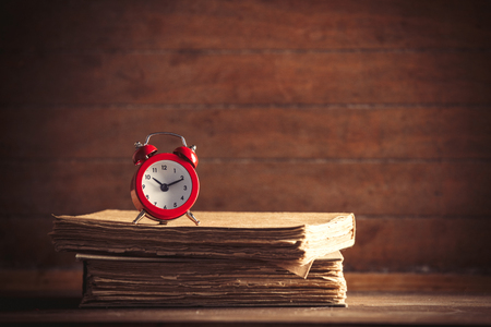 Little alarm clock and books on wooden background. image in old color styleの写真素材