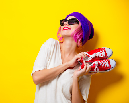 Young girl with pink hair in purple hat and sunglasses holding a red gumshoes on yellow backgroundの写真素材