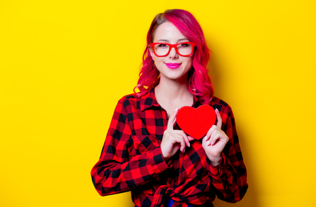 Young pink hair girl in red tartan shirt with red heart shape box. Portrait isolated on yellow backgroundの写真素材