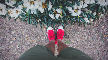 Male foots in red gumshoes near bush flowers in park. Up side viewの写真素材