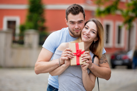 Young couple, brunet man and blonde girl, with gift box in the european city old town. Summertime seasonの写真素材