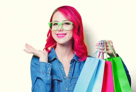 Young pink hair girl in blue shirt and green glasses holding a colored shopping bags.の写真素材