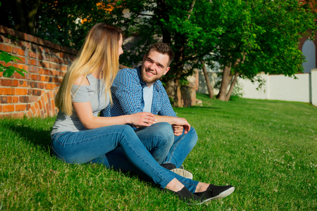Young couple sitting on a green grass in the city in summertime.の写真素材