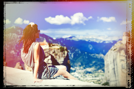 photo of the beautiful young woman sitting on the stone railing and looking at the splendid view in Greece. Image with film old frame.の写真素材