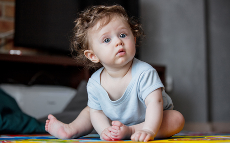 little curly baby boy sitting at floor in loft flat.の写真素材
