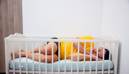 Young tired father sleep in a child cot at home.の写真素材