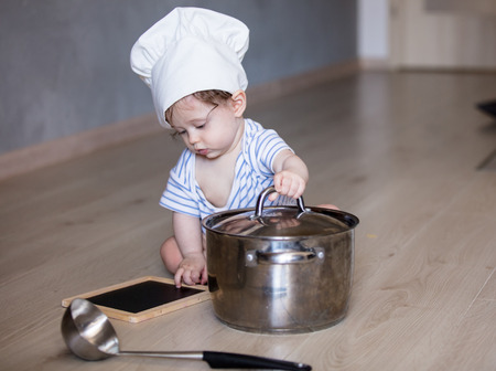 Little child boy in chef hat on a floor with pot and ladleの写真素材