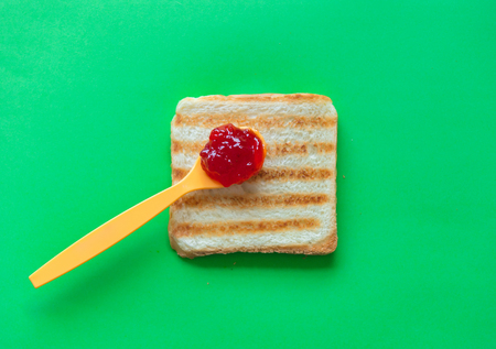 Slice of toast bread and tea spoon with jam on green background, top viewの写真素材