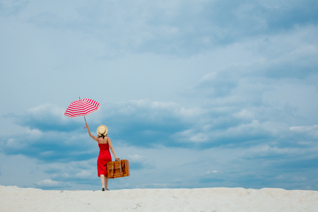 Young woman in red dress with umbrella and suitcase on the beach. Travel concept image on sandの写真素材