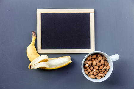 White cup full of almond with banana near blackboard on grey background. Above viewの写真素材