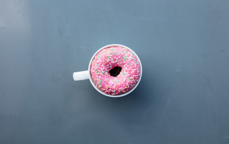 Cream donut in a cup on grey metal background. Above view