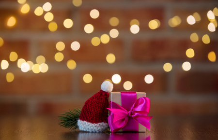handmade gift box with purple bow and Santa Claus little hat on wooden table with fairy lights on bokeh backgroundの写真素材