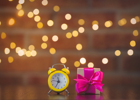 handmade gift box with purple bow and alarm clock on wooden table with fairy lights on bokeh backgroundの写真素材