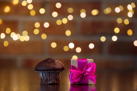 handmade gift box with purple bow and chocolate cupcake on wooden table with fairy lights on bokeh backgroundの写真素材