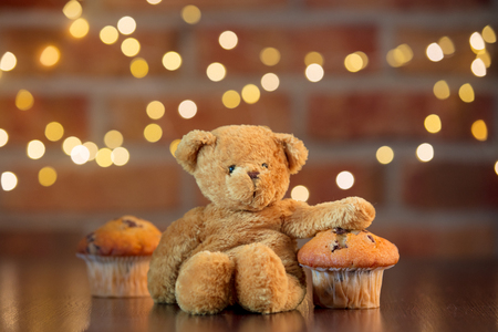 Real homemade classic cupcakes and teddy bear. Fairy lights and gift box in bokeh background. Christmas time conceptの写真素材