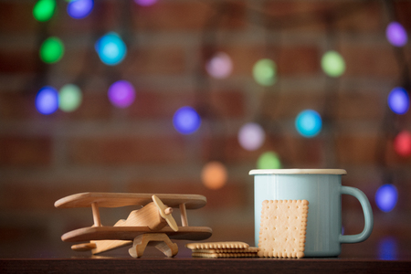 Hot cup of coffee, cookie and wooden plane with fairy lights on background. Christmas seasonの写真素材