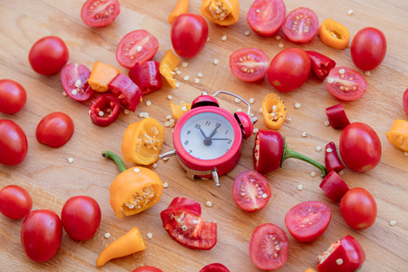 yellow and red peppers, tomatoes with alarm clock on wooden table. Above viewの写真素材