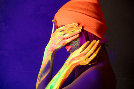 Young girl in hat with fluorescent paint on lips and face. Studio shot.の写真素材