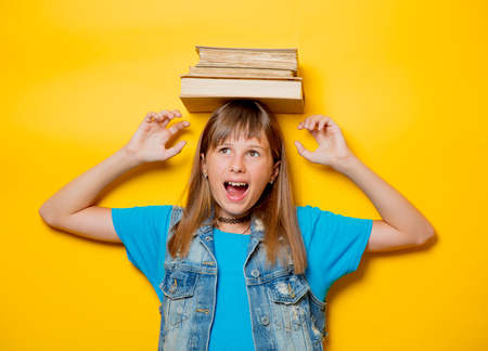 portrait of young teenage girl with books on yellow background