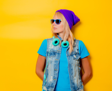 portrait of young trendy girl in hat and headphones on yellow backgroundの写真素材