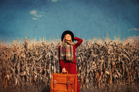 Young girl coat with suitcase on a rural road near cornfield. Image in old dirty paper styleの写真素材
