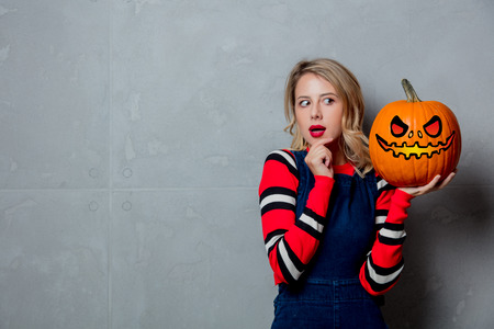 Portrait of a young style blonde girl in red striped sweater with halloween pumpkin on grey background.の写真素材