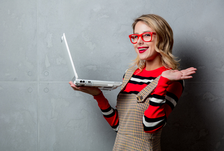 Portrait of a young style blonde girl in red striped sweater with laptop computer on grey background.の写真素材