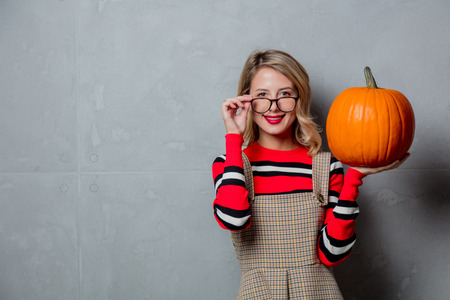 Portrait of a young style blonde girl in red striped sweater with halloween pumpkin on grey background.の写真素材