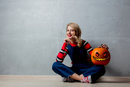 Portrait of a young style blonde girl in red striped sweater with halloween pumpkin on grey background.の写真素材