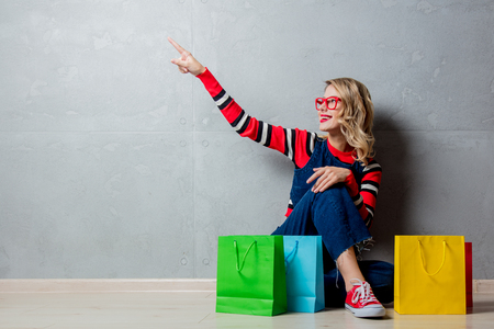 Young style girl in jeans clothes sitting with shopping bags on grey background.の写真素材