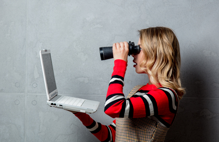 Young girl with laptop computer and binoculars on grey backgroundの写真素材