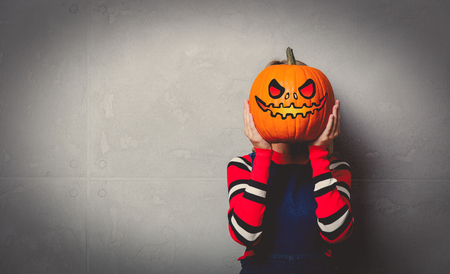 Portrait of a young style blonde girl in red striped sweater with halloween pumpkin on grey background.の写真素材