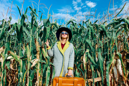 Young girl in coat with suitcase on a cornfield. Image in old dirty paper styleの写真素材