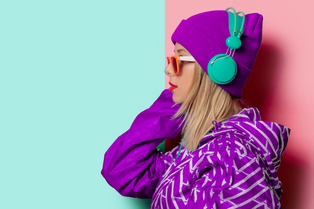 Young blonde girl in 90s sports jacket and hat on pink and blue background.の写真素材
