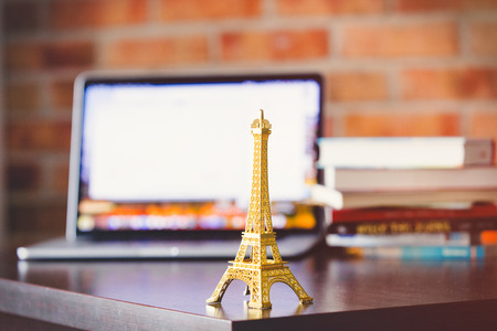 Little golden Eiffel tower on a table with laptop computer and books on brick wall background