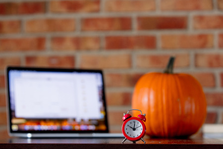 Little alarm clock on a table with pumpkin on brick wall background