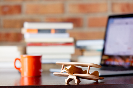 Wooden airplane toy on a table with books and laptop computer on brick wall backgroundの写真素材