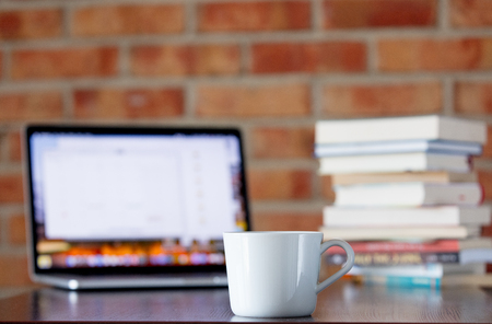 Cup of coffee and laptop computer on a table with books on brick wall backgroundの写真素材