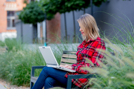 Portrait of a young beautiful girl with notebook computer sitting at bench near a house.の写真素材