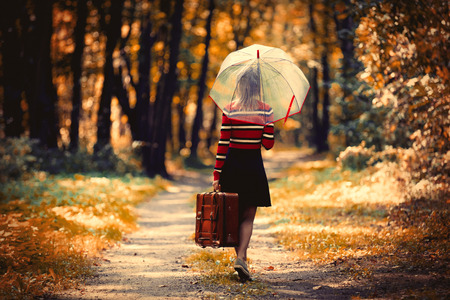 Young girl with umbrella and suitcase in park in autumn seasonの写真素材