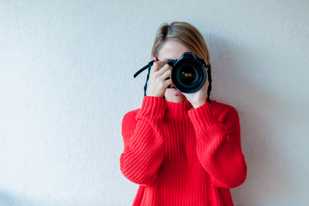 Young girl in red sweater and glasses with professional camera on white backgroundの写真素材