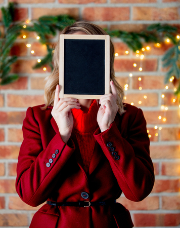 Portrait of a young girl in red coat with blackboard at Christmas lights backgroundの写真素材