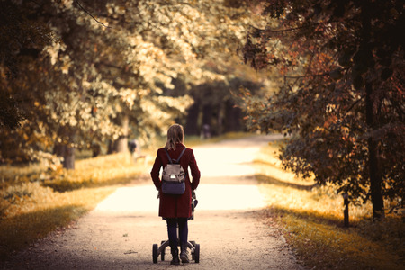 Young woman strolling in a park with stroller and a child in autumn seasonの写真素材
