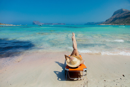 Young redhead girl in black bikini and with hat lying down on lounger on Balos beach, west Crete, Greece. Summertime season vacation, Julyの写真素材