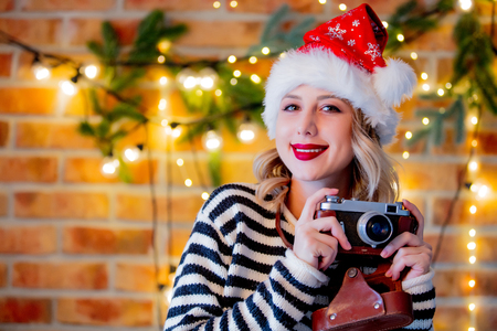 Portrait of a young cozy woman with vintage camera Christmas lights and pine branchの写真素材