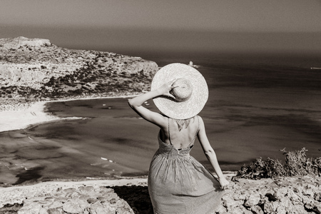 Young redhead girl in hat and dress with sea coastline on Balos, Crete, Greece